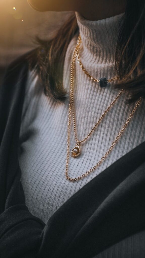 Close-up of layered gold necklaces worn over a ribbed sweater for a chic fashion statement.