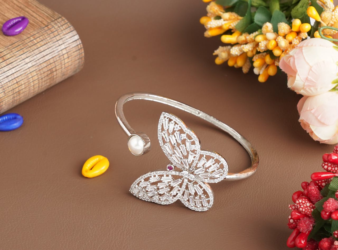 Stylish butterfly bracelet with pearl on a brown surface adorned by colorful beads and flowers.